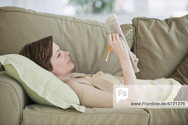 Woman lying on sofa with newspaper