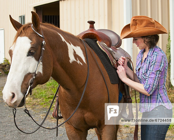 Woman putting saddle on horse