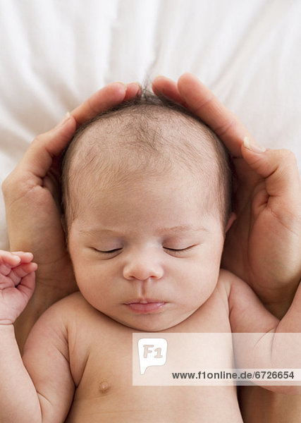 Parent's hands wrapped around sleeping baby's head