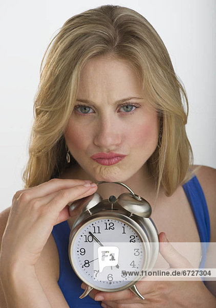 Upset blond woman holding an alarm clock