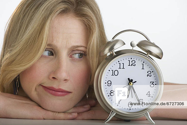 Worried blond woman looking at alarm clock
