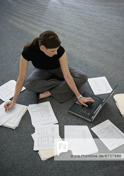 Woman sitting on floor with laptop with documents around