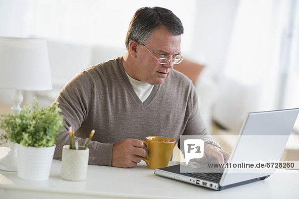 USA  New Jersey  Jersey City  Man using laptop  holding drink in living room