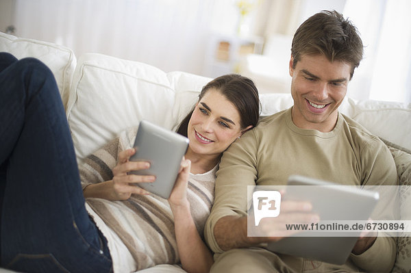 Couple sitting on sofa  using digital tablets