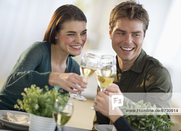 Couple toasting with white wine with third party in background