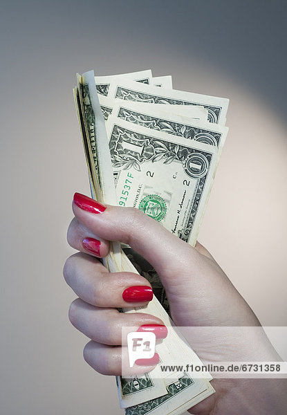 Close up of woman's hand with red nail polish holding bunch of dollar banknotes