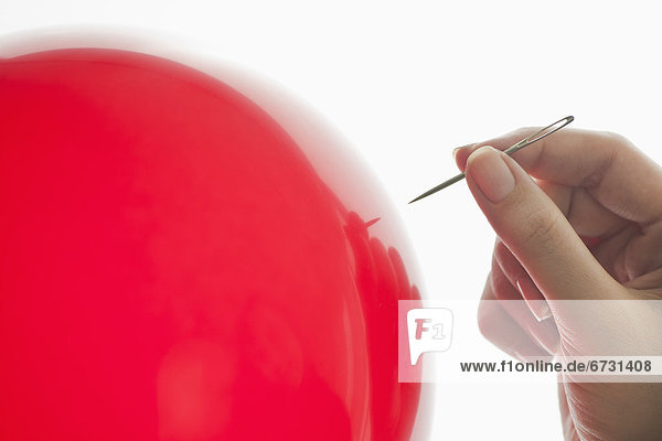 Studio shot of woman holding needle close to red balloon