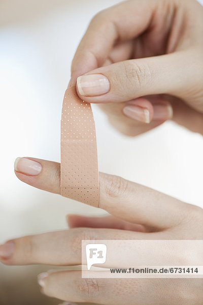 Studio shot of woman sticking adhesive bandage on finger