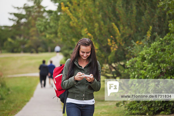 'Young Woman Walking On A Path In A Park Checking Text Messages