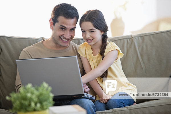 Daughter (8-9) and father sitting on sofa and using laptop