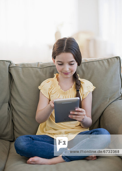 Girl (8-9) sitting on sofa and using digital tablet