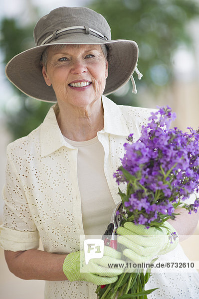 Portrait of smiling senior woman wearing gardening gloves  holding bunch of purple flowers
