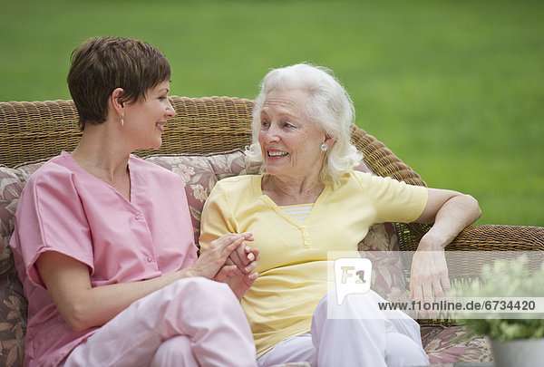 Senior woman and nursing assistant relaxing on outdoor sofa