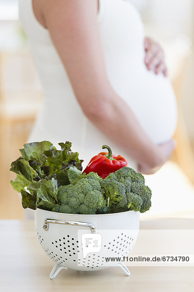 Fresh vegetables in colander  pregnant woman in background