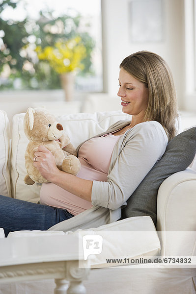 Young pregnant woman on sofa with teddy bear
