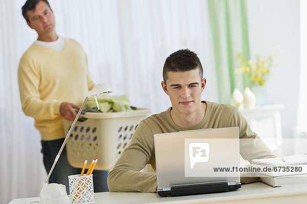 Son (16-17) using laptop being observed by father