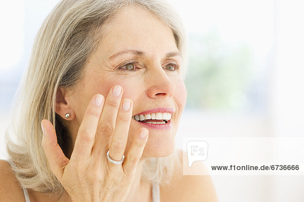 Portrait of senior woman applying moisturizer