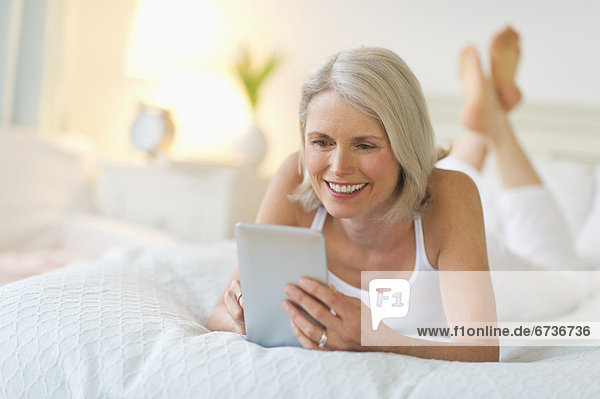 Senior woman lying on bed and using digital tablet