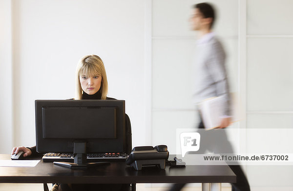 Businesswoman working on computer  businessman walking in background