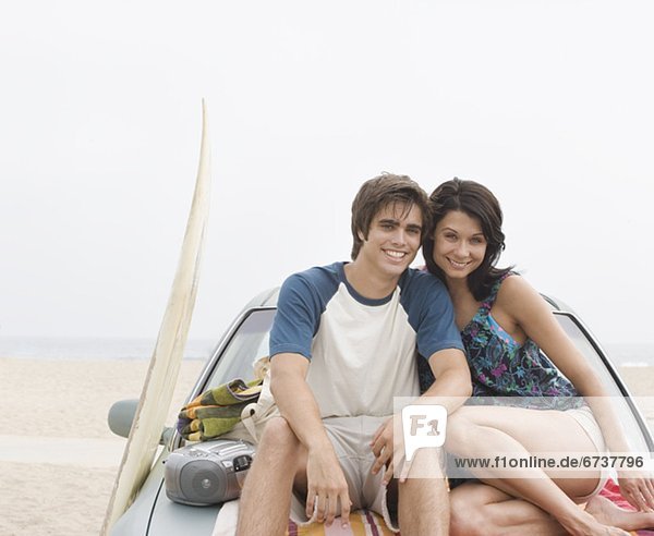 Couple sitting on hood of car at beach