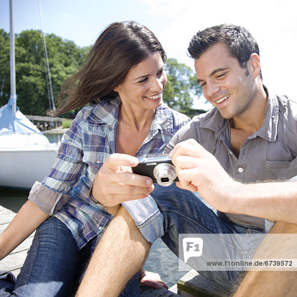 Couple sitting on dock looking at photos on digital camera