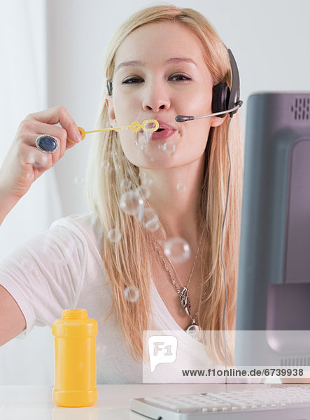 Young female telephonist blowing bubbles at work