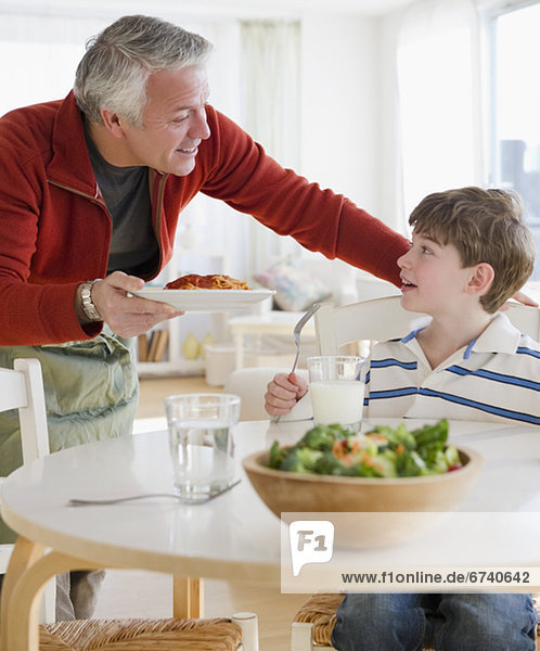 Father giving plate of spaghetti to son