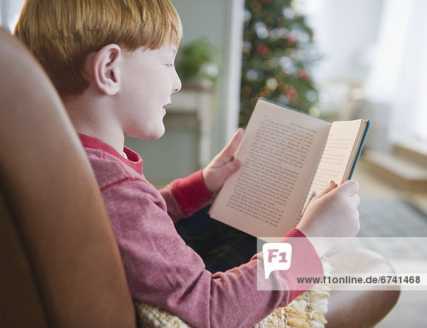 Boy (8-9) reading book on Christmas Eve