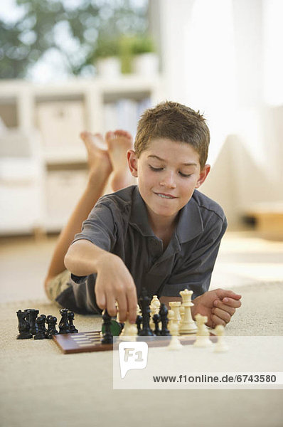 Boy (10-11) lying on floor and playing chess