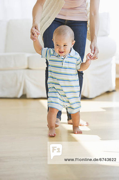 Mother helping son (6-11 months) with first steps