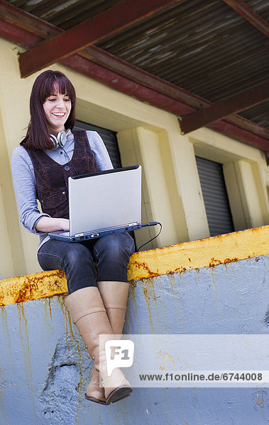 USA  New Jersey  Jersey City  young woman sitting on wall using laptop