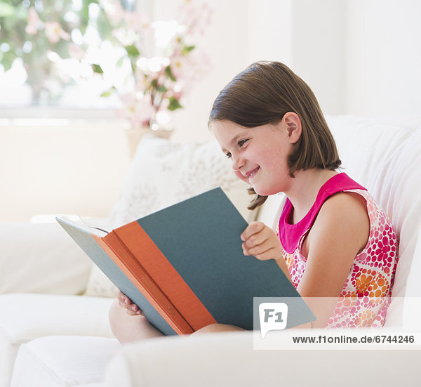 Close up of girl (6-7) reading book on sofa
