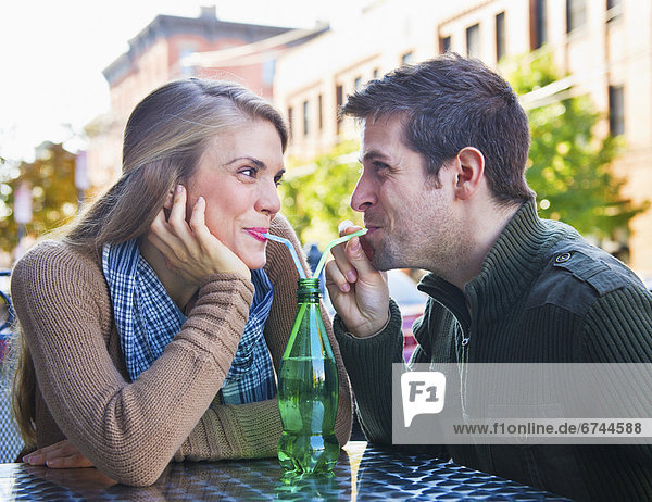 Young couple drinking from one bottle using straws
