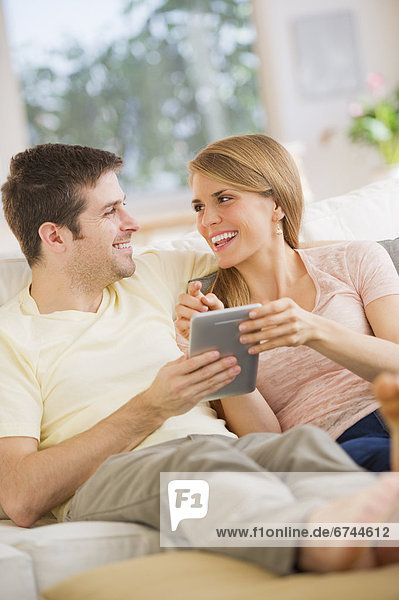 Young couple sitting on sofa with digital tablet