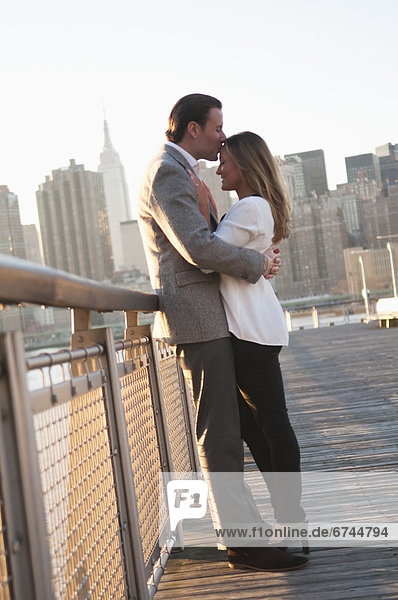 USA  New York  Long Island City  Young couple kissing on boardwalk  Manhattan skyline in background