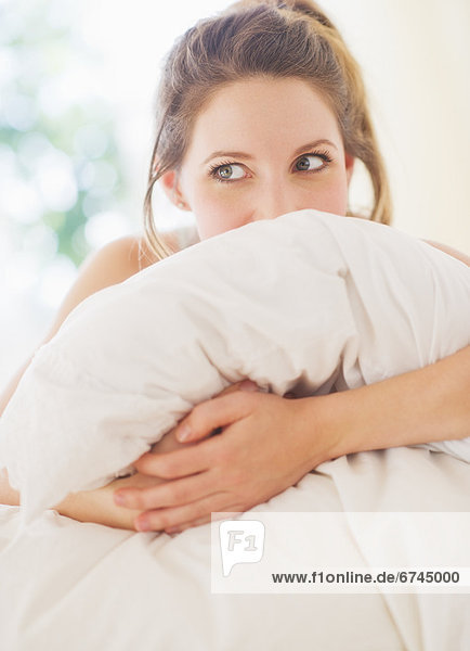 Portrait of young woman embracing pillow in bedroom