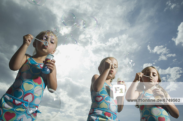 Three young sisters blowing bubbles