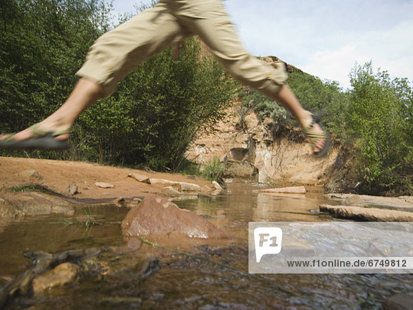 Woman jumping over stream