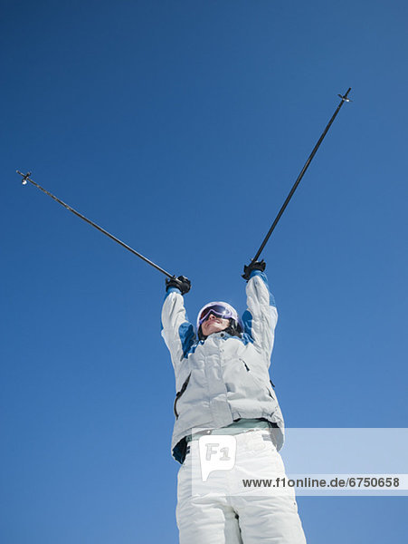 Woman holding ski poles over head