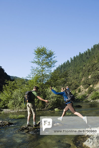 Hikers jumping across river on rocks