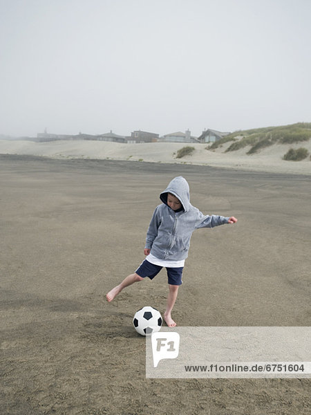 Boy kicking soccer ball on beach