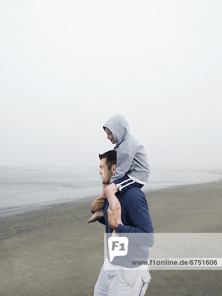 Father carrying son on shoulders on beach