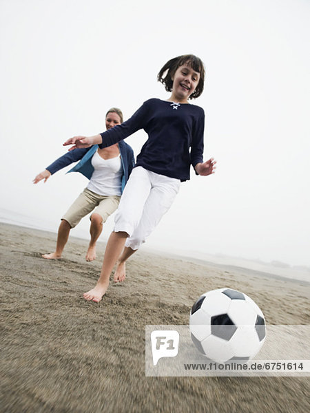 Mother and daughter playing soccer on beach