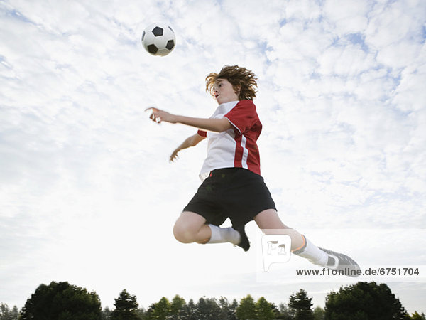 Boy jumping toward soccer ball in mid-air
