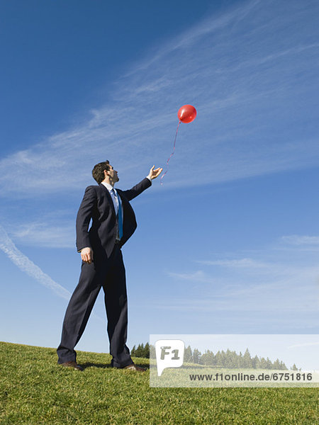 Businessman letting red balloon go