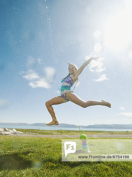Girl (8-9) jumping over watering system