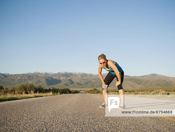 USA  Utah  Kanosh  Mid adult woman taking break from running on empty road