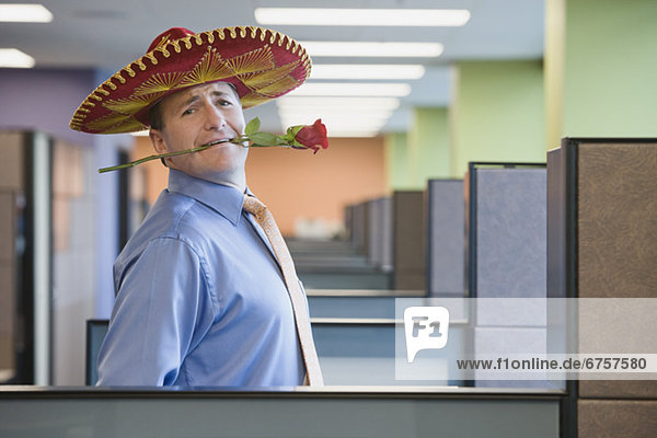 Businessman wearing sombrero and holding rose in teeth