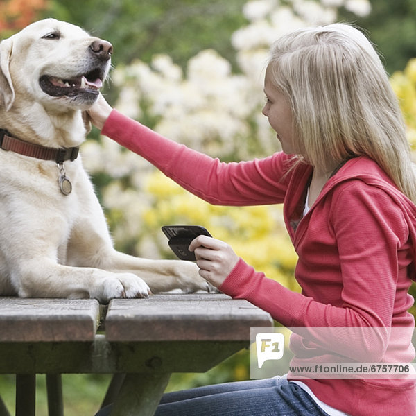 Girl petting dog sitting on picnic table