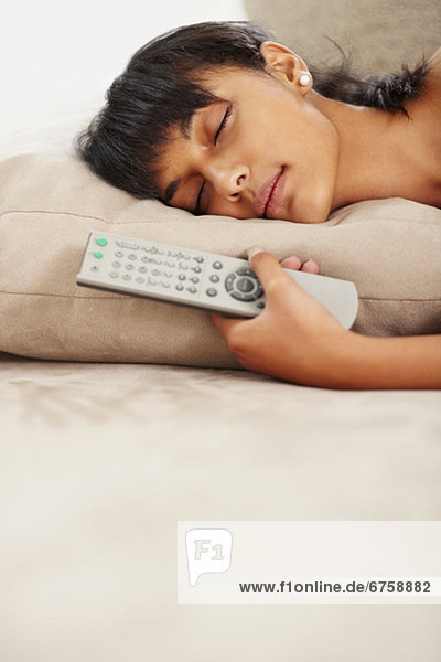 Young woman holding remote control while sleeping